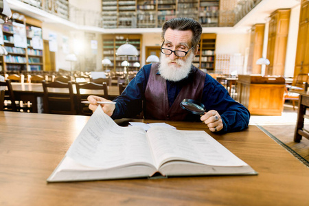 一位聪明伶俐的老教授，穿着时髦休闲的复古服装坐在古图书馆的桌子旁看书。教育图书馆理念