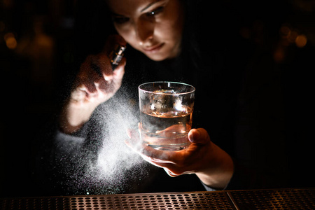 女人用一只手拿着盛着饮料的玻璃杯，然后喷在上面。