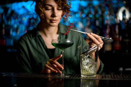 酒吧里的年轻女子拿着盛着鸡尾酒的玻璃杯，精确地装饰着它