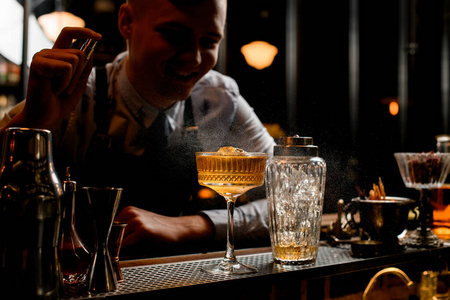 年轻微笑的酒吧招待在玻璃杯上洒上冰镇酒精饮料