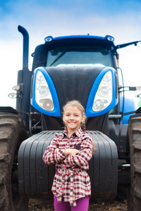 一个可爱的女孩，在田间的现代拖拉机旁。