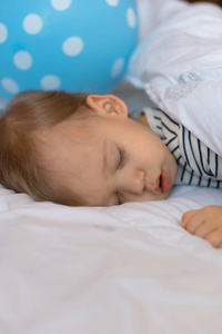 金发的小宝宝睡在他的床上，背景是蓝色的球