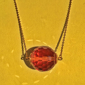 Gold chain with a pendant of sultanite on a yellow background. 