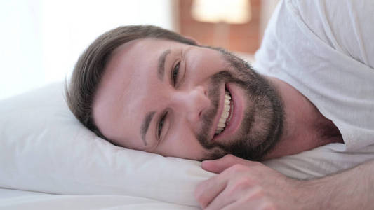 特写镜头，一个留着快乐胡须的年轻人在床上对着镜头微笑