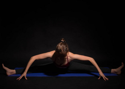 一个年轻的女运动家在黑暗的背景下在垫子上做瑜伽
