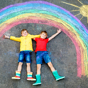 在大流行性冠状病毒隔离期间，两名小学生在地上用彩色粉笔画上彩虹。孩子们在画彩虹的同时画上单词让一切都好起来。