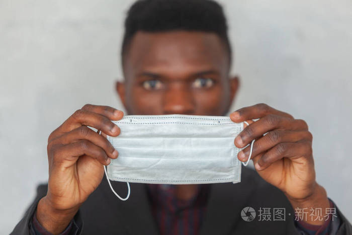 科维德19一名年轻的非洲男子双手拿着一个防护性的医用面罩以防感染