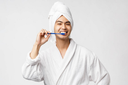 美容水疗和休闲理念。乐观快乐的亚洲人，穿着浴衣和浴巾，用牙刷刷牙，面带微笑，注意个人卫生，白底
