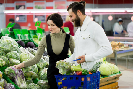 一对健康夫妇在超市购物时看着水果和蔬菜的肖像。一对漂亮的夫妇在超市挑选卷心菜。
