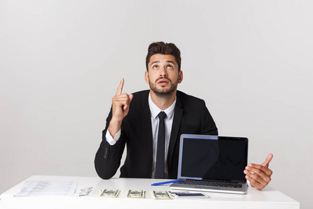 商业理念穿着西装的帅哥商人坐在办公室里用手指指着复印空间，笔记本电脑被隔离在灰色背景上。