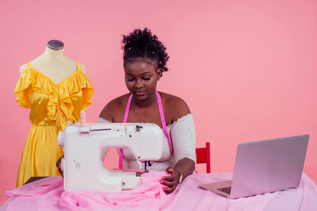 在工作室的复制区，一位漂亮的女裁缝站在模特旁边，粉红色的背景上有缝纫机。观念与灵感