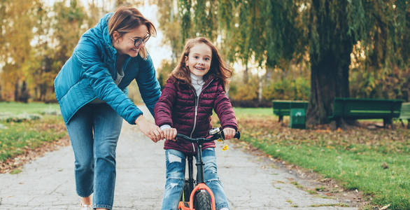 迷人的中年母亲戴着眼镜教她的小女孩骑自行车