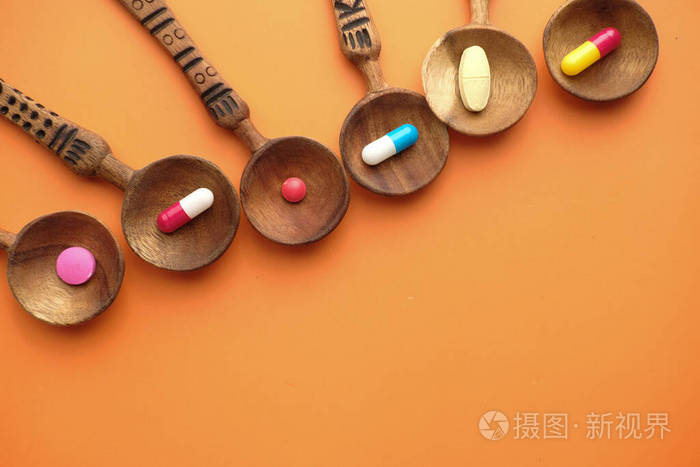 橙色背景下汤匙上的药丸和胶囊特写镜头