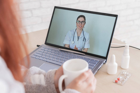 一位感冒的妇女正在休病假，正疯狂地看医生的笔记本电脑视频会诊。远程预约的病人。在线会议。