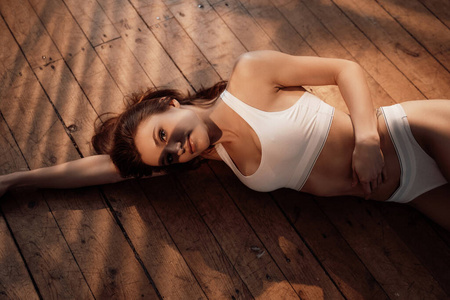 照片中一个几乎模特穿着运动内衣，在公寓的木地板上放松