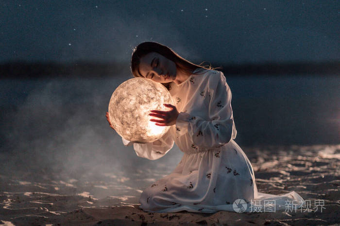 美丽的年轻女孩在沙滩上沙滩上星光灿烂手里拿着月亮