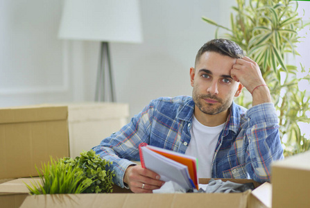 一个搬家的男人坐在空荡荡的公寓的地板上，在箱子中间，检查着清单上的东西