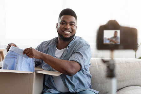 解装箱Vlog。微笑的黑人男子在镜头前打开箱子和新衣服