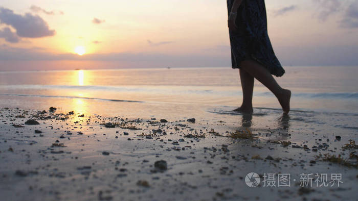 沙滩上的女人腿夕阳下漫步在海边沙滩上的女孩海滩旅行暑假概念