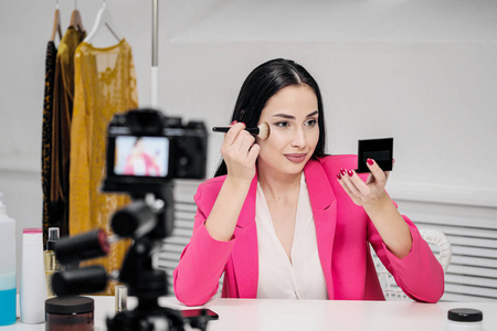 一位穿着粉色夹克的漂亮年轻女博主拍摄了一篇关于化妆品的博客。