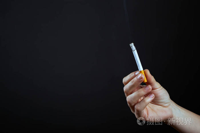 手拿着一支点燃的香烟背景是黑色的尼古丁和烟草的危害