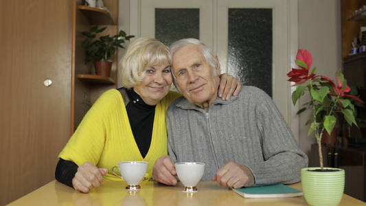 幸福的老爷爷奶奶夫妇坐在家里的桌子上，一起喝茶