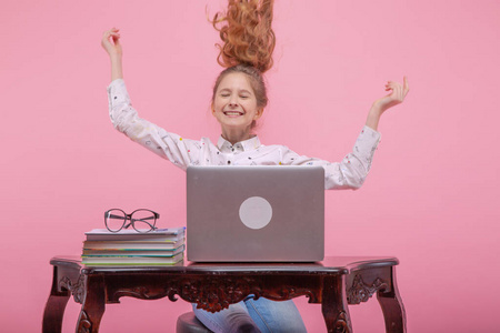 美丽的年轻女孩摇曳着金色长发，微笑着靠近笔记本电脑。在粉红色的背景上。