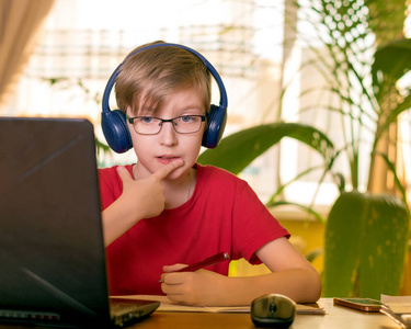 金发男孩戴着耳机在桌旁做作业