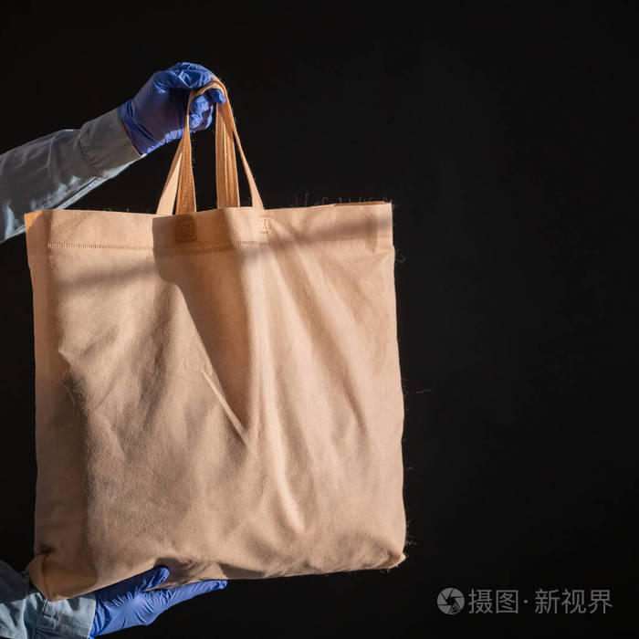 黑底棉布袋快递员拿着一个黑色背景上没有塑料包装的帆布布袋安全运送