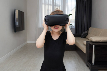 十几岁的女孩戴着虚拟现实眼镜，戴着耳机，玩着虚拟现实盒子。技术，新一代，进步理念。女孩试图触摸虚拟现实中的物体。