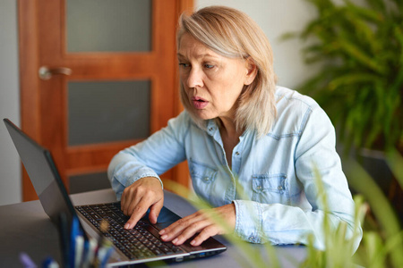 成熟的女人在家里看着笔记本电脑。