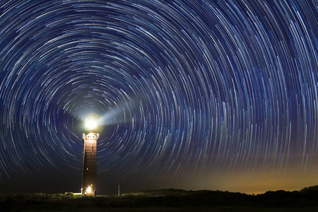 夜晚灯塔中央有星光轨迹图片