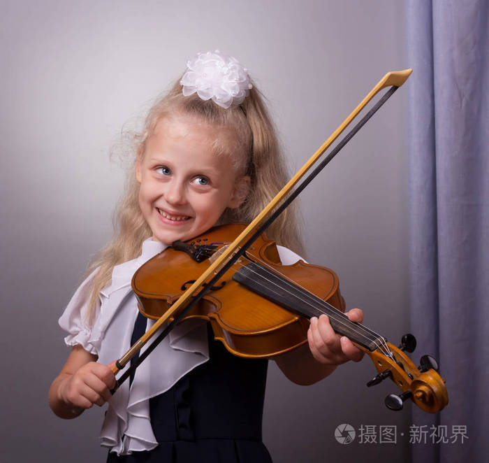 快乐的小女孩在灰色背景上拉小提琴