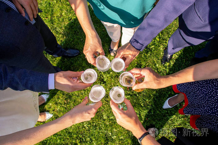 人们手里拿着盛着白葡萄酒的玻璃杯婚礼派对朋友们在公园里喝香槟敬酒