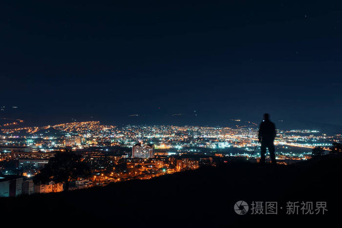 大城市的夜晚.摄影师的剪影站在城市的山顶上,进行夜间摄影.