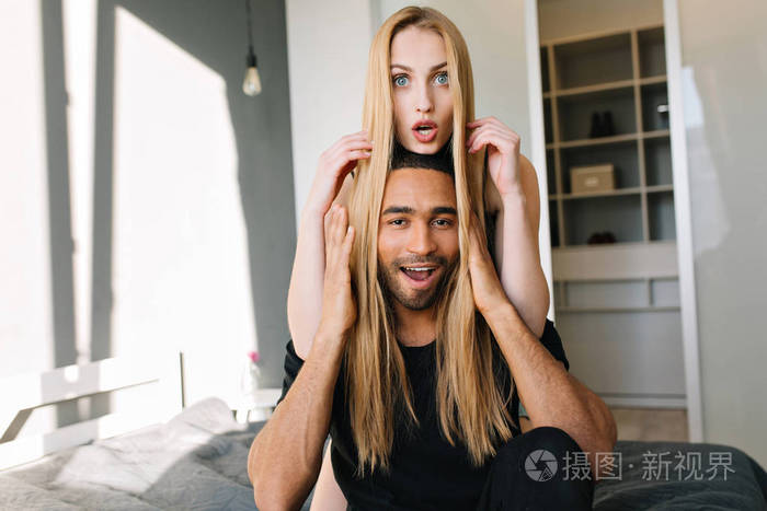 一对漂亮的金发美女和一个快乐的帅哥在现代公寓的床上玩得很开心快乐