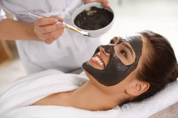 美容美容师在spa美容院为女性面部敷上黑色面膜
