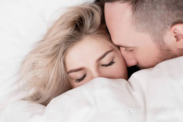 这对夫妻男人和女人躺在床上拥抱着睡在白色的被褥上把他们的脸藏在