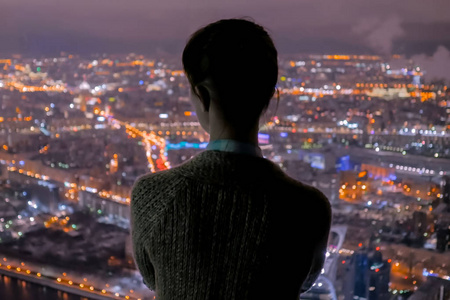 沉思的女人从摩天大楼望着夜市图片