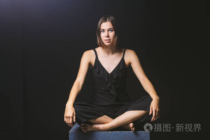 女孩穿着黑色连衣裙坐在黑暗的墙上.