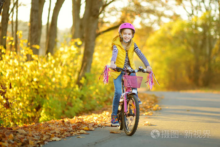 在阳光明媚的秋日一个可爱的小女孩在城市公园里骑自行车积极的家庭