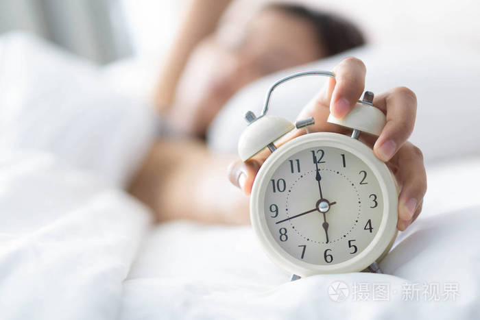 特写女人睡在床上手拿闹钟起床时间到了