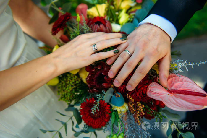 新婚夫妇手牵手展示结婚戒指特写婚礼花束背景上的手和戒指
