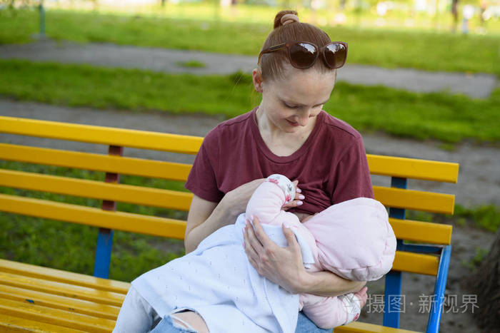 一位妇女正在公园里的长凳上给婴儿喂奶春日
