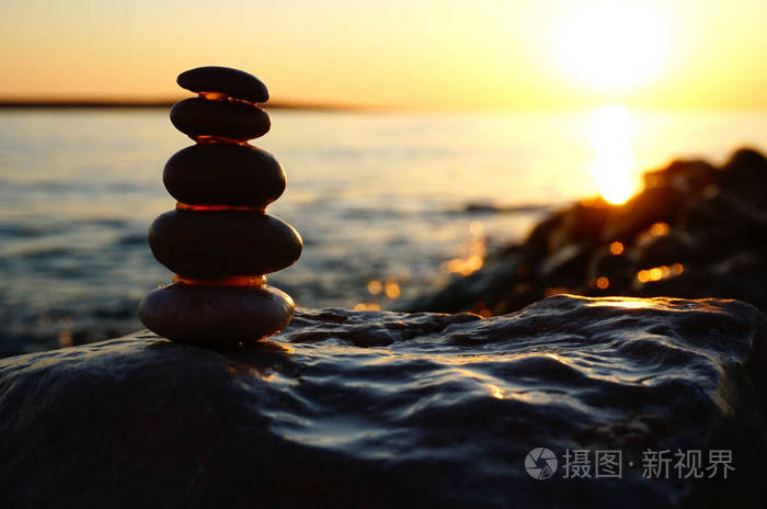夏日海上夕阳的背景与鹅卵石海滩和堆叠的石头剪影在太阳前面