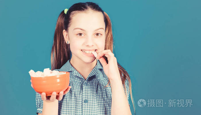 热量和饮食.女孩笑脸捧碗甜棉花糖在手蓝色背景.
