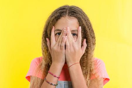 肖像关于十几岁的女孩窥视通过手指.黄色的工作室波黑