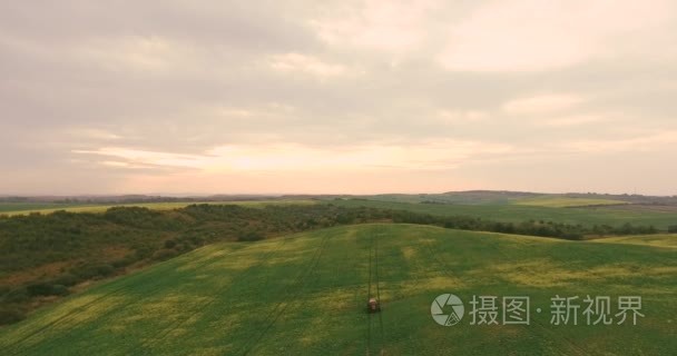 航拍视频拖拉机设备施肥喷雾农业油菜作物植物场附近森林在日落