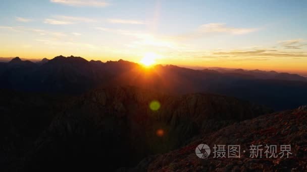 游戏中的山峰落日时光倒流。太阳落在尖峰的阿尔卑斯山。粉色紫色的天空。多彩的 flare 在相机镜头