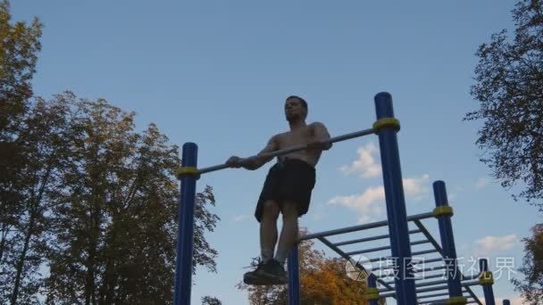 强壮的肌肉男人做肌肉 ups 在一个公园里。年轻运动员做引体向上单杠室外上。健身肌肉男在夏天室外训练。拉起的运动员。锻炼体育生活